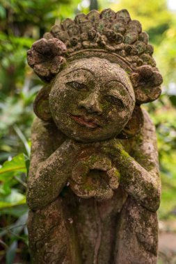 Bali 'nin geleneksel zanaatkarlığının huzur ve sanatsal özünü yansıtan, yemyeşil bir yeşil ile çevrili huzurlu, yosun kaplı bir Balili taş heykel..