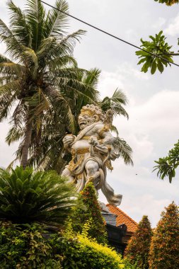 Görkemli bir beyaz ve altın tapınak koruyucu heykeli palmiye ağaçları ve tropikal yapraklara karşı dimdik ayakta duruyor. Balili ruhani mimarisinin ihtişamını temsil ediyor.
