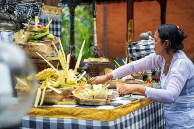 Bali, Endonezya - 29 Kasım 2023: Geleneksel giyinmiş bir Balili kadın tapınak sunağında tütsü ve canlı süslemelerle tören hazırlıyor..