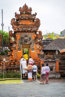 Bali, Indonesia - November 30, 2023: Worshippers ascending temple stairs beneath a majestic candi bentar gate, its terracotta walls adorned with classic Balinese architectural elements clipart