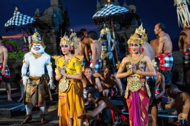 Bali, Endonezya - 23 Kasım 2023: Altın kostümlü Balili sanatçılar Kecak dansı sırasında zarif poz verdiler, Hanuman ve ilahi söyleyen adamlar gece gökyüzünün altında antik bir tapınak yarattılar..