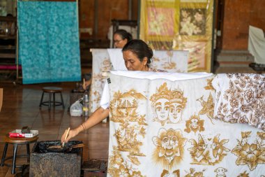 Bali, Endonezya - 23 Kasım 2023: Balili bir sanatçı, yerel bir atölyede geleneksel mitoloji motiflerinin yer aldığı karmaşık batik desenler yaratarak, kumaşa sıcak balmumu uygular..