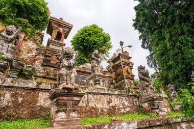 Eski taş muhafızları Bali tapınağı kompleksini gözlüyor. Karmaşık oymalar ve geleneksel mimari karışımı gür tropikal bitki örtüsüyle vahşi ifadeli koruyucu heykeller olarak