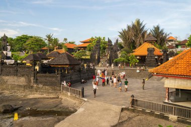 Bali, Endonezya - 11 Kasım 2023: Koyu taş kapılı ve turistlerin geleneksel beyaz elbiseli turistlerin bulunduğu turuncu çatılı özgün Bali mimarisine sahip sakin kıyı tapınağı kompleksi