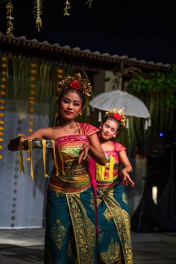 Bali, Endonezya - 11 Kasım 2023: İki Balili kadın, Bali 'de sakin bir açık havada geleneksel müzik eşliğinde canlı dans hareketleri sergiliyor.