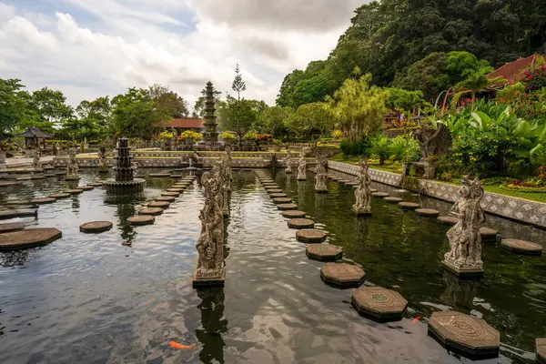 Geometrik basamak taşları olan kutsal su bahçesi, geleneksel heykeller ve verimli tropikal yapraklar ve geleneksel Bali mimarisi ile çevrili merkez çeşmesi..