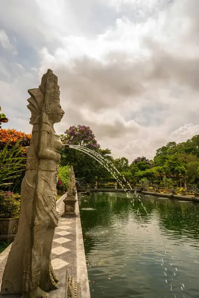 Tiran Gangga 'daki zümrüt havuzlara su püskürten entrika oyulmuş taş tanrısı. Süslü Balili heykel, bu kutsal su bahçesinde dramatik bulutlu gökyüzüne karşı nöbet tutuyor..