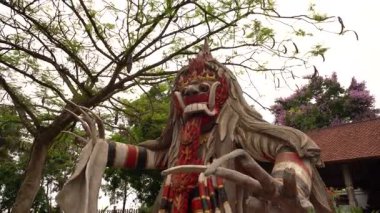 Renkli Balili iblis maskeli heykel. Vahşi bir ifade ve dalgalı saçlar geleneksel tapınak bahçesinde.