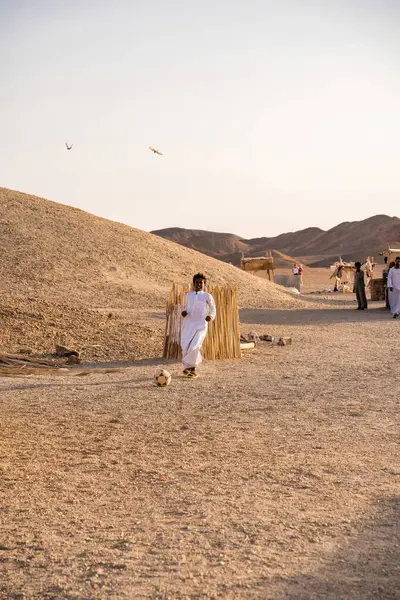 Kahire, Mısır - 11 Eylül 2023: Geleneksel giyinmiş bir adam Mısır 'da sakin bir çöl manzarasının ortasında futbol maçının keyfini çıkarıyor.