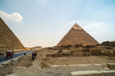 Antik Mısır piramitlerinin gezginleri ve ön planda bir yolu olan manzaralı bir perspektifi.