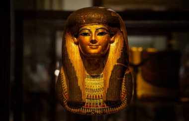 Bir müzede kaplanmış ve Nil medeniyetinin mirasını yansıtan altın detaylarıyla ve sembolik motifleriyle özenle hazırlanmış bir antik Mısır maskesi.