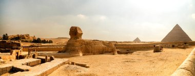 Giza, Mısır 'daki Sfenks ve piramitlerin panoramik manzarası. Ufuk çizgisine uzanan altın kumlar ve antik kalıntılar..