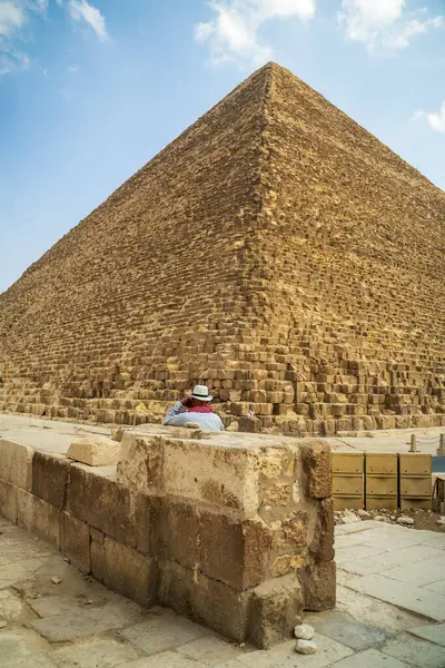 Büyük Giza Piramidi 'nin yanında canlı mavi gökyüzünün altında oturan bir gezgin bu antik Mısır simgesinin anıtsal ve tarihsel önemini yakalıyor..