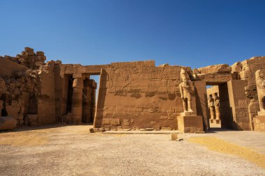 Luxor 'daki antik Mısır tapınağı kalıntıları temiz çöl gökyüzü altında firavun heykelleri, hiyeroglif duvarlar ve kumtaşı mimarisini gösteriyor..