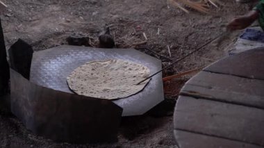 Kırsal bir ızgarada pişen geleneksel yassı ekmek, geleneksel mayasız ekmeği eski ahşap bir tahta üzerinde merdaneyle hazırlayan kişinin yakın çekimi, zanaat süreci..