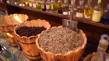 Kurutulmuş otlar ve baharatlarla dolu büyük ahşap varillerin ve çeşitli şişe yağlarının bulunduğu canlı bir pazar tezgahı.