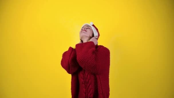 穿着圣诞圣塔帽的年轻而积极的女人被黄色的背景隔离了 戴着圣诞礼帽的快乐的年轻女子在跳舞 人与寒假概念 — 图库视频影像