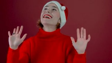 Noel Baba şapkalı genç pozitif kadın kırmızı arka planda izole edilmiş. Noel Baba şapkalı mutlu genç kadın. İnsanlar ve kış tatili konsepti