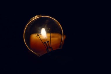 Yanan bir mumun arka planındaki ampulü kapattım. Kesinti. Enerji krizleri. Karartma konsepti.. 