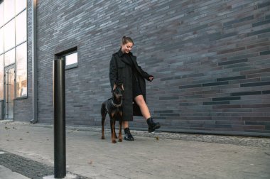 Doberman 'ın yanındaki kadın. Şehrin sokaklarında köpeğini gezdiren genç bir kadın. Köpekli genç kız.