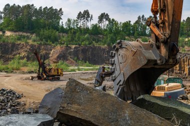 Bazalt madenciliği. Ormanın yakınındaki bazalt ocağında sarı kazıcılar. Açık hava madeninde büyük bir turuncu kazıcı.