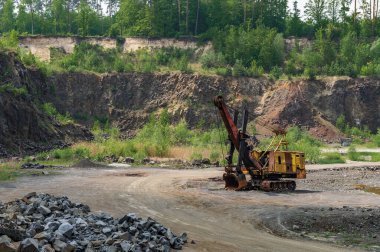 Bazalt madenciliği. Ormanın yakınındaki bazalt ocağında sarı kazıcılar. Açık hava madeninde büyük bir turuncu kazıcı.
