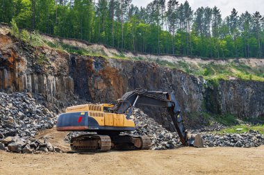 Bazalt madenciliği. Ormanın yakınındaki bazalt ocağında sarı kazıcılar. Açık hava madeninde büyük bir turuncu kazıcı.