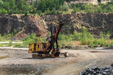 Ormanın yakınındaki bazalt ocağında kazıcılar var. Açık hava madeninde büyük bir turuncu kazıcı. Bazalt madenciliği. 