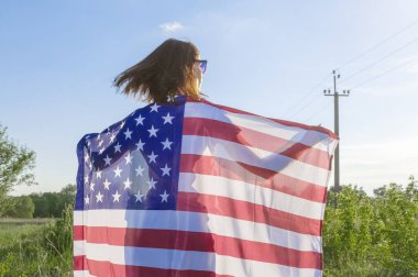 Arka tarafta elinde Amerikan bayrağı olan bir kadın var. Amerikan bayrağı taşıyan genç bir kadın. ABD Bağımsızlık Günü Kutlaması. 