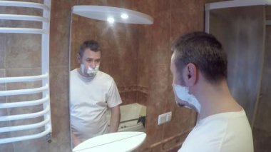 Banyoda sakalını tıraş eden yakışıklı bir adam. Adam aynanın önünde tıraş oluyor.