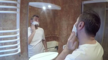 Banyoda sakalını tıraş eden yakışıklı bir adam. Adam aynanın önünde tıraş oluyor.