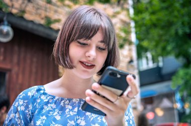 Açık kafede cep telefonu olan genç bir kız. Kafede akıllı telefonuyla oturan güzel kız.
