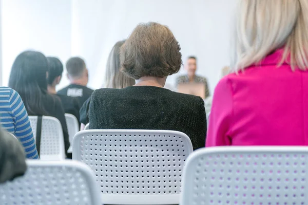 People listening to a conference in a meeting room. Rear view of unrecognized participant in audience. Audience of students or workers.