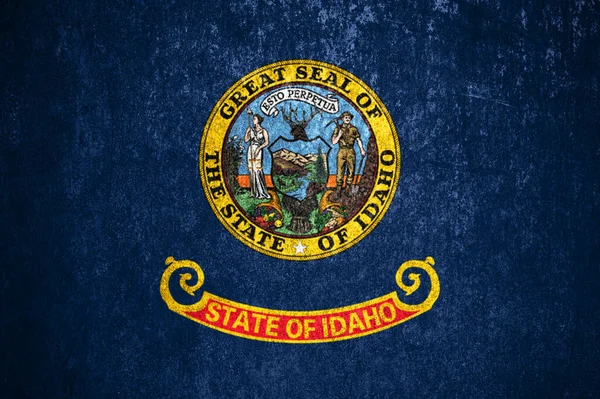 Close-up of the grunge Idaho state flag. Dirty Idaho state flag on a metal surface.