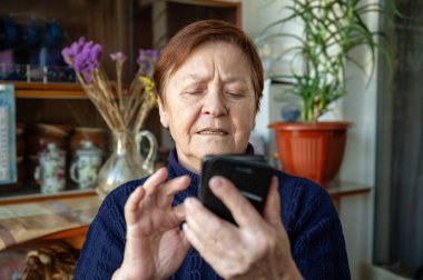 Akıllı telefon kullanan yaşlı bir kadının portresi. Pencerenin yanındaki yaşlı kadın cep telefonu kullanıyor.