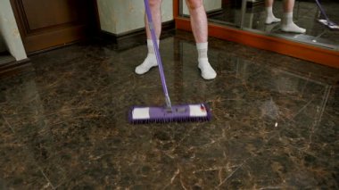 Çalışkan adam hızlı ev işi yapıyor ve seramik zemini temizliyor. Yerleri yıkıyorum. Elinde paspas olan bir adam bir apartmanın seramik zeminini yıkıyor. Evin temizliğini sağlama konsepti..