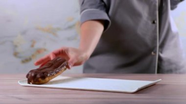 Koyu çikolata jöleli Fransız tatlısı. Fırında Fransız eklerini tabağa koyan bir kadın. Tabakta kremalı ev yapımı ekler var... 