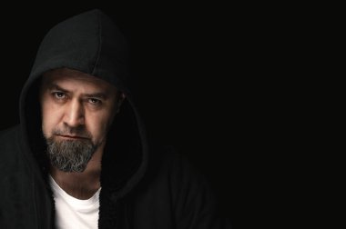 Karanlık arka planda kapüşonlu gizemli bir adam. Siyah arka planda siyah kapüşon giyen yakışıklı bir manken.