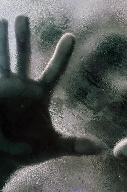 Elleri buzlu cama bastırılmış insan figürü. Mat camın arkasında bir adamın gölgesi bulanık el ve yumuşak vücut odağı. Özgürlük kavramı