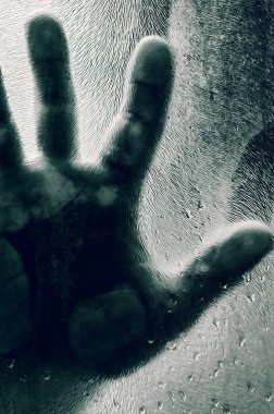 Elleri buzlu cama bastırılmış insan figürü. Mat camın arkasında bir adamın gölgesi bulanık el ve yumuşak vücut odağı. Özgürlük kavramı