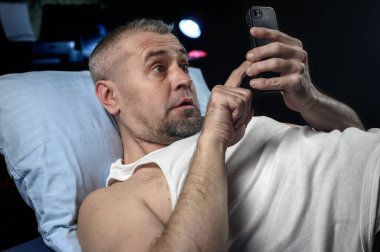 Geceleri yatakta akıllı telefonu olan bir adam. Gergin, şok olmuş, endişeli bir adam yatakta yatarken telefonuna bakar. Uykusuzluk ve uyku bozuklukları kavramı.