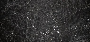 Dalgalı siyah su. Defocus, berrak, berrak, durgun su yüzeyi dokusunu su sıçramaları ve kabarcıklarla bulanıklaştırdı. Su yüzeyi arkaplanı