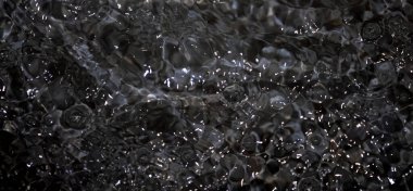 Dalgalı siyah su. Defocus, berrak, berrak, durgun su yüzeyi dokusunu su sıçramaları ve kabarcıklarla bulanıklaştırdı. Su yüzeyi arkaplanı