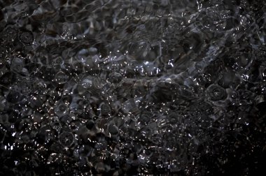 Dalgalı siyah su. Defocus, berrak, berrak, durgun su yüzeyi dokusunu su sıçramaları ve kabarcıklarla bulanıklaştırdı. Su yüzeyi arkaplanı