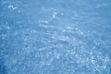 Dalgalı mavi su. Defocus, berrak, durgun su yüzeyi dokusunu su kabarcıkları ve kabarcıklarla bulanıklaştırdı. Su yüzeyi arkaplanı