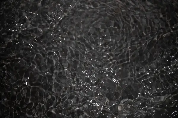 Dalgalı siyah su. Defocus, berrak, berrak, durgun su yüzeyi dokusunu su sıçramaları ve kabarcıklarla bulanıklaştırdı. Su yüzeyi arkaplanı