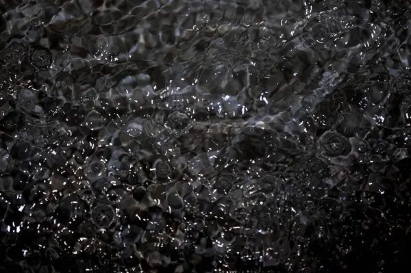 Dalgalı siyah su. Defocus, berrak, berrak, durgun su yüzeyi dokusunu su sıçramaları ve kabarcıklarla bulanıklaştırdı. Su yüzeyi arkaplanı