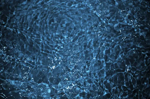 Dalgalı mavi su. Defocus, berrak, durgun su yüzeyi dokusunu su kabarcıkları ve kabarcıklarla bulanıklaştırdı. Su yüzeyi arkaplanı