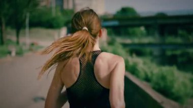 Şehirde nehir kenarında koşan genç bir kadın. Kadın geriye doğru koşuyor. Koşu yaşam tarzı sağlıklı yaşam tarzı.