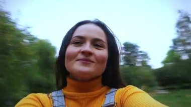 Parkta dönen mutlu genç bir kadın. Neşeli ve heyecanlı genç güzellik gülüyor ve gülümsüyor, bir kamera tutuyor, dönüyor, selfie çekiyor ve hayalleri için çabalıyor..